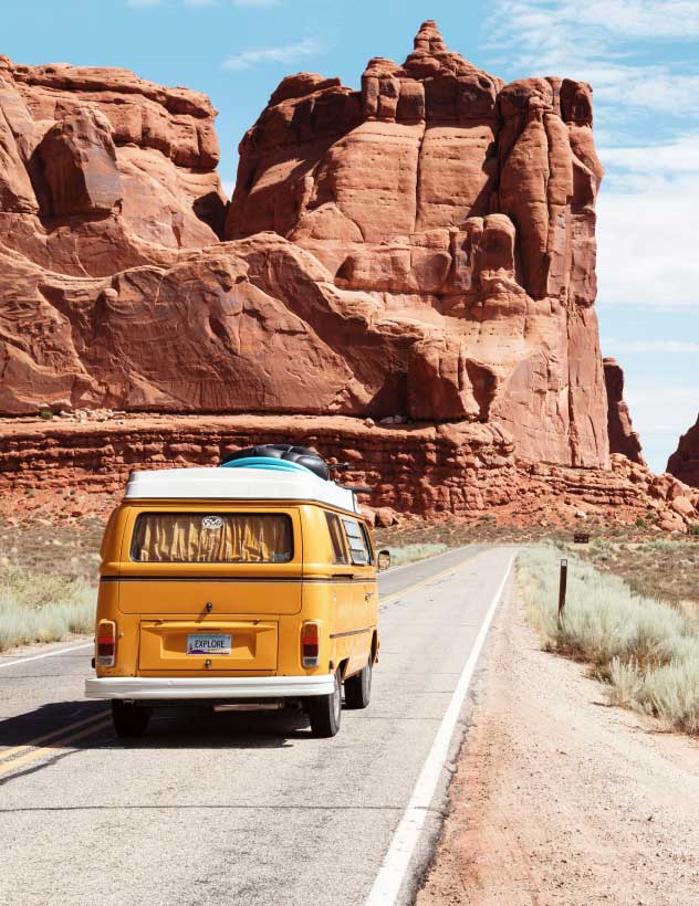 Photo of orange VW bus with EXPLORE license plate driving in desert.Photo by Dino Reichmuth on Unsplash